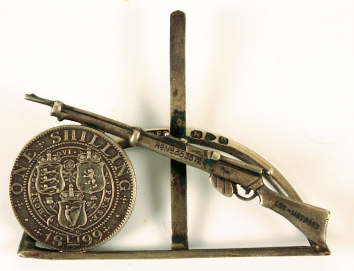 Great Britain 1899 shilling mounted in a silver clip with a representation of a Lee Metford rifle, and an enamelled George IV shilling at Whyte's Auctions