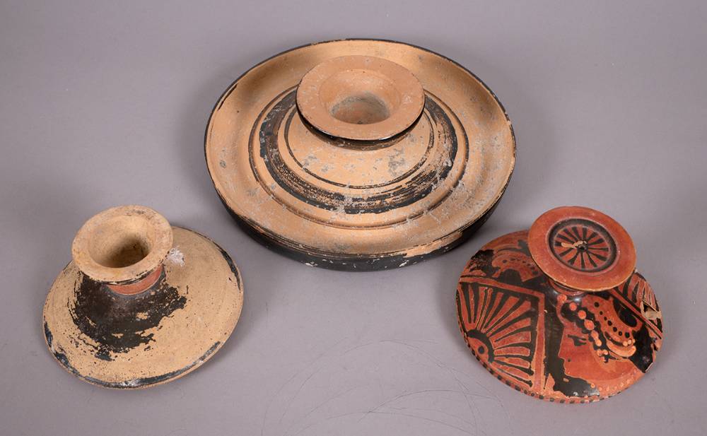 Circa 300BC South Italian style candle holder and two pot lids. at Whyte's Auctions